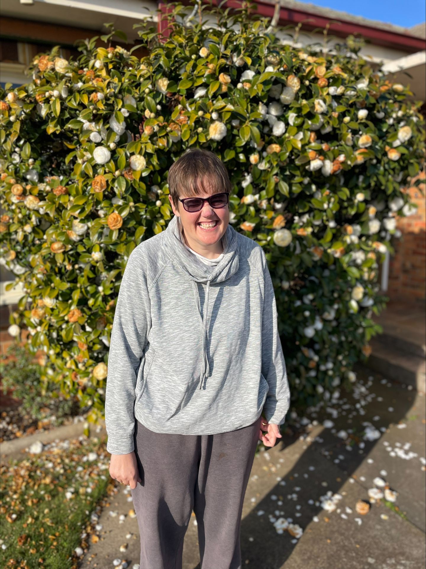 A Four Point Therapy Participant smiling outdoors in front of a flowering camellia
